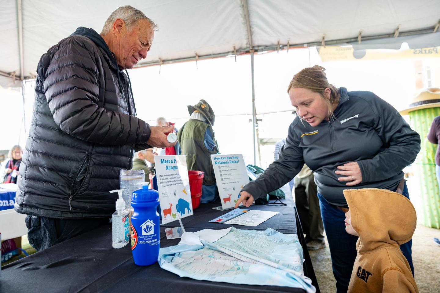 Man and woman at booth with pamphlets, engaging with a child in a hoodie.