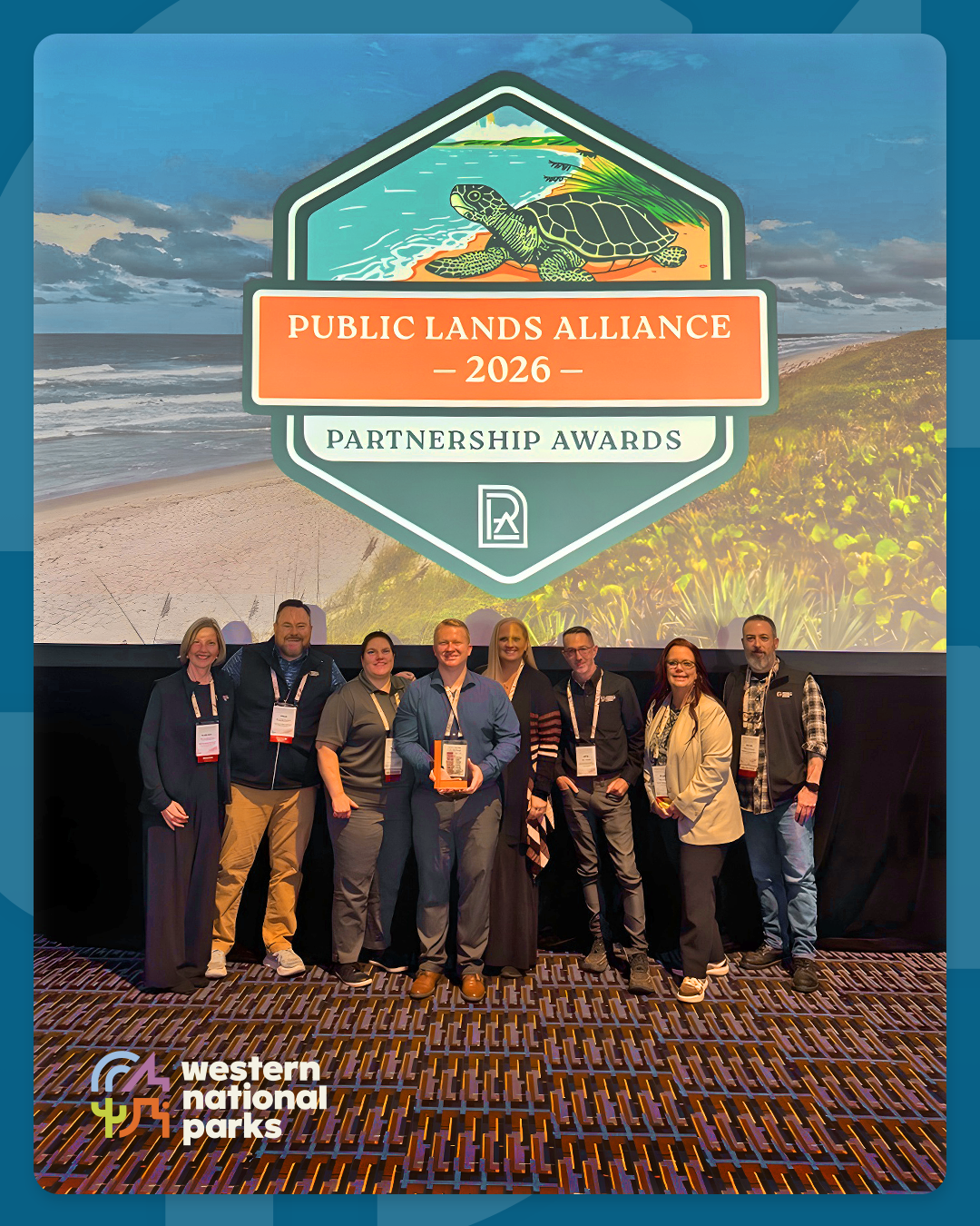 Group of people posing with an award in front of a large logo display.