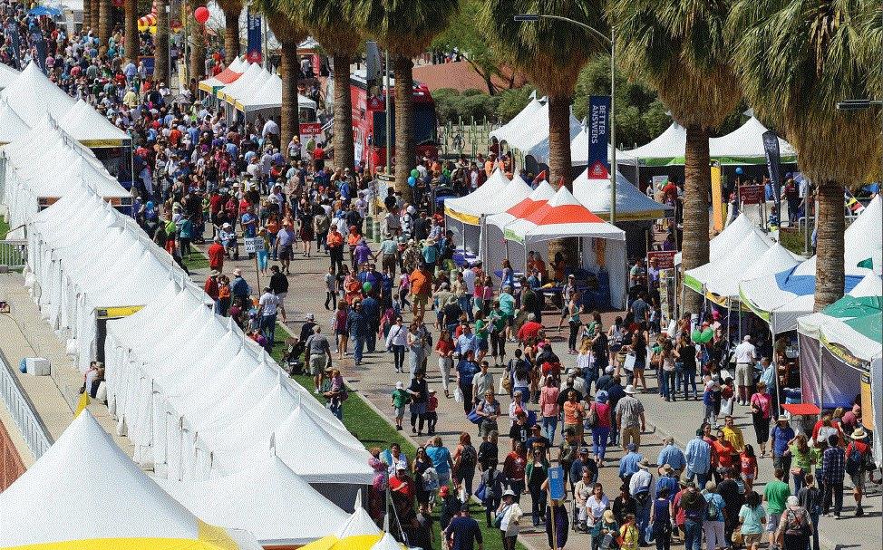 Crowded street fair with tents, palm trees, and many people.