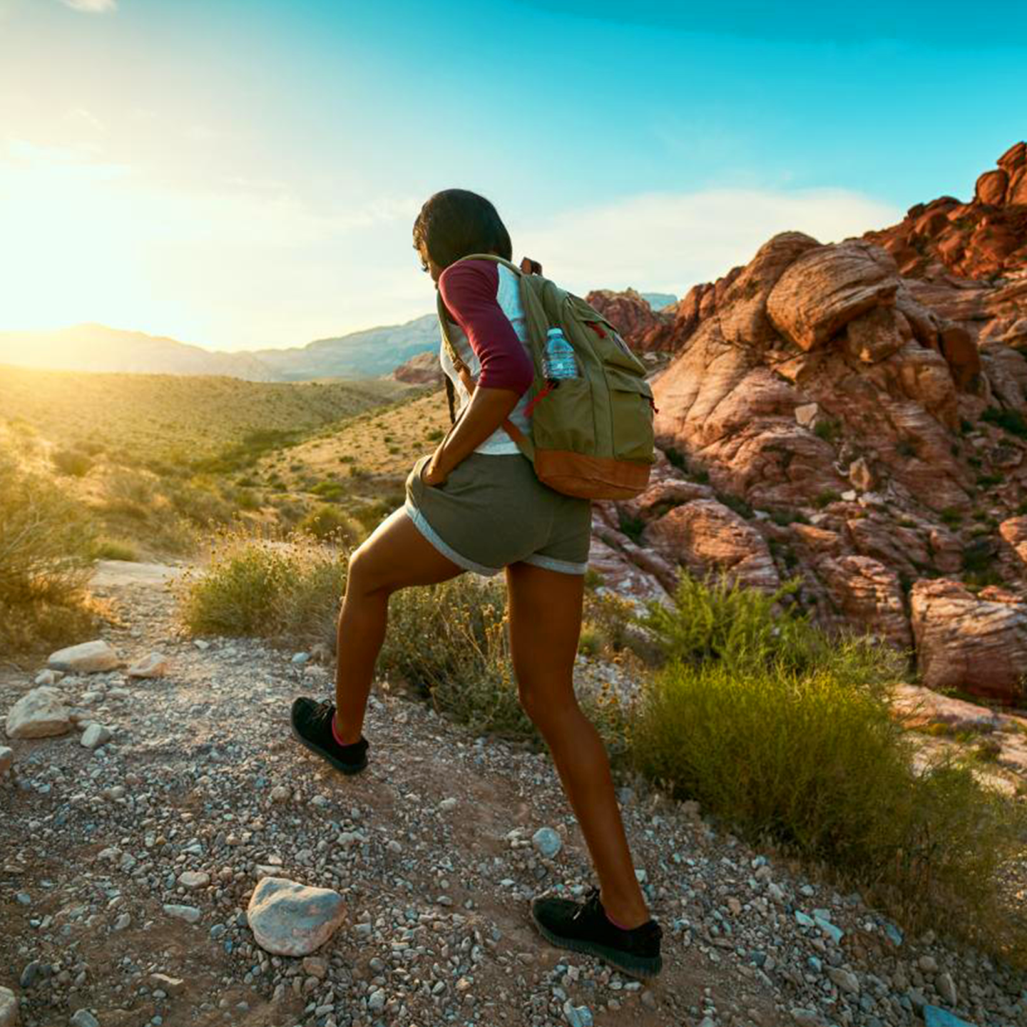 Hiker in the desert at sunrise with red rocks and clear sky.