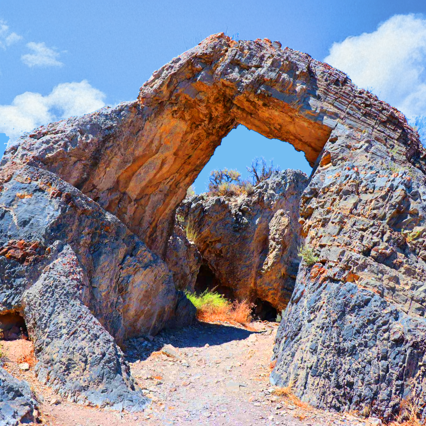 Rock arch formation under a blue sky with scattered clouds.