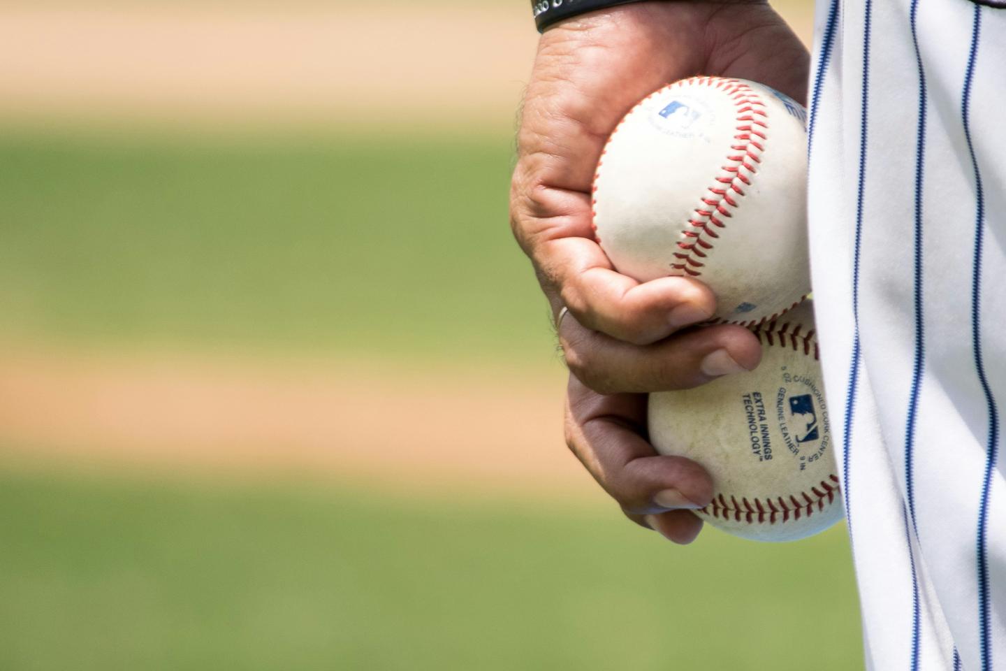 Hand holding three baseballs on a field.