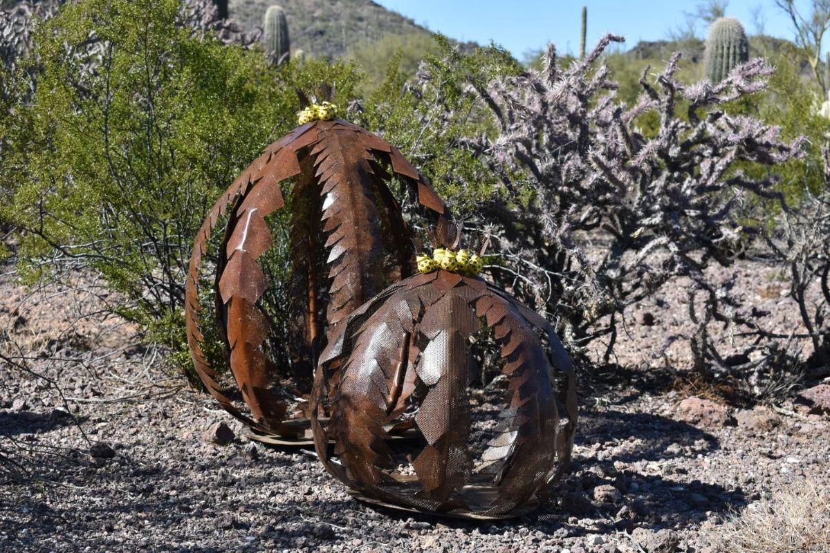Rustic metal sculptures of pumpkins in a desert landscape with cacti.
