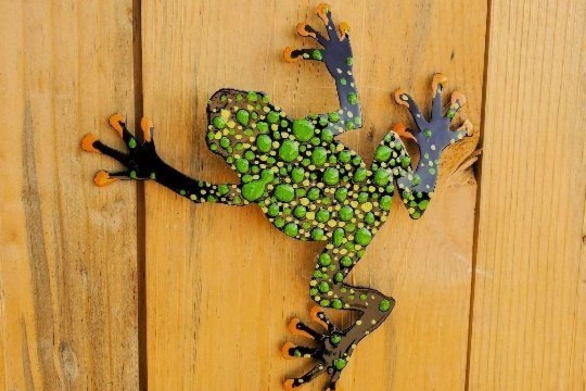 Colorful frog sculpture climbing wooden surface.