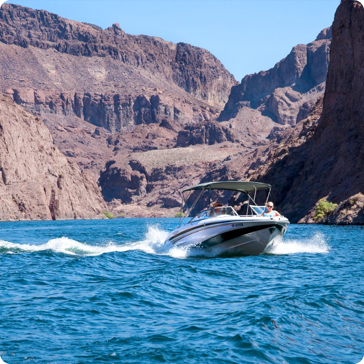 Boat speeding on a blue river between rocky cliffs under a clear sky.
