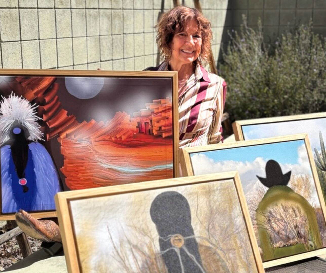 Person smiling, standing behind colorful paintings displayed outdoors.