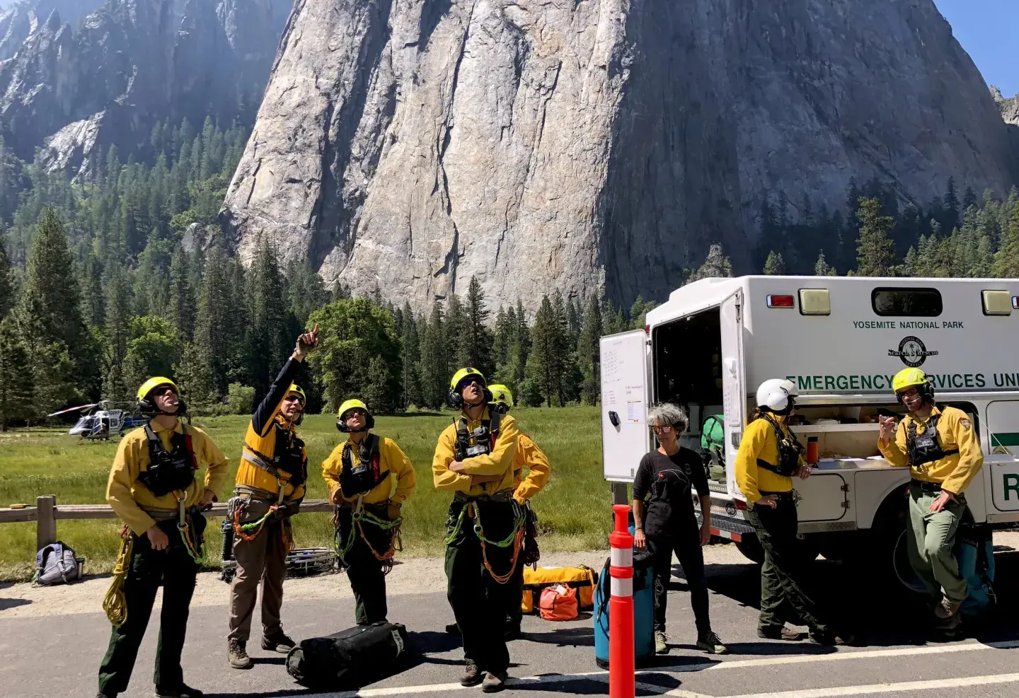 Firefighters in yellow uniforms stand by a rescue truck near a mountainous landscape.