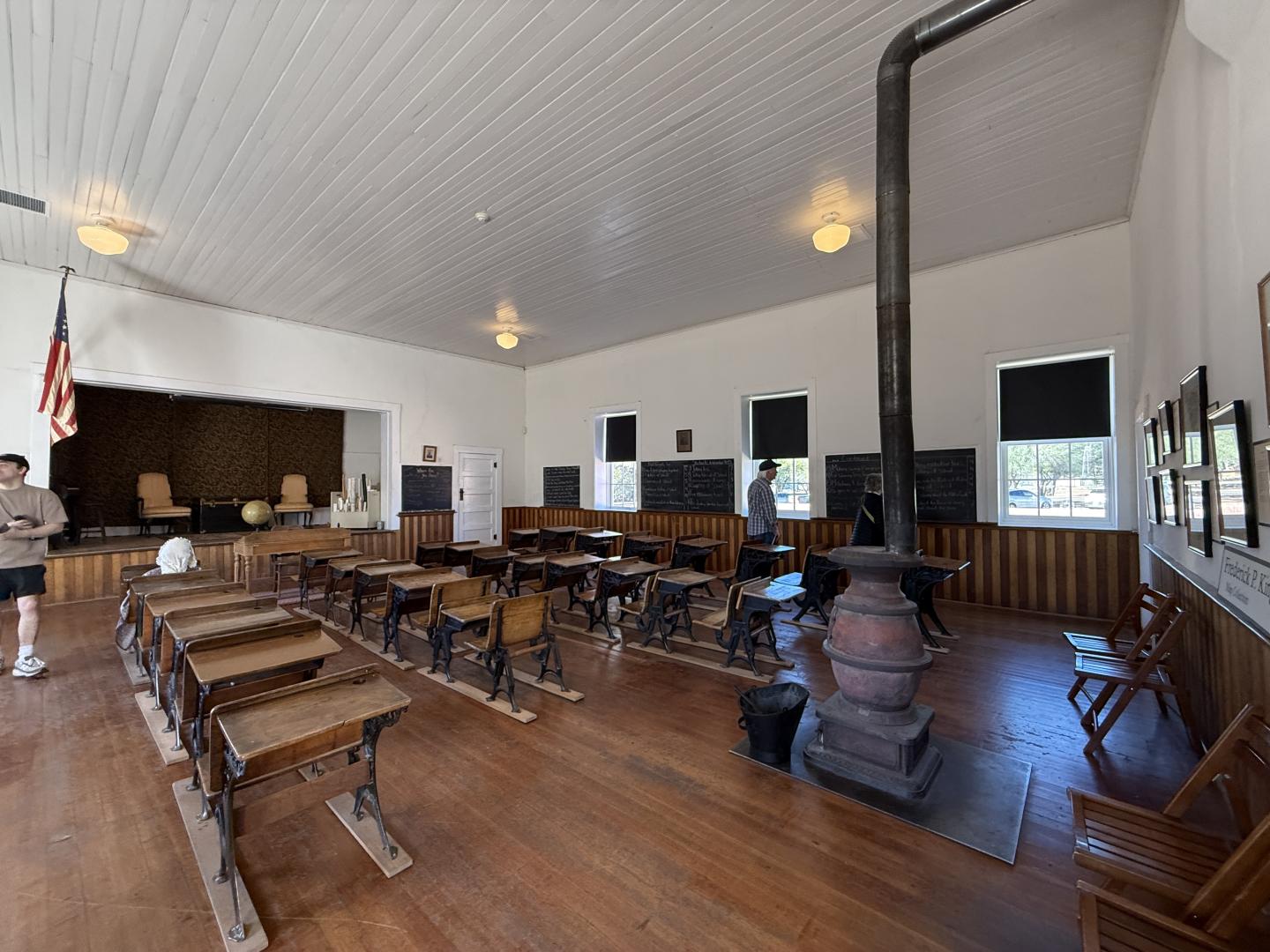 Old classroom with wooden desks, a stove, blackboards, and an American flag.