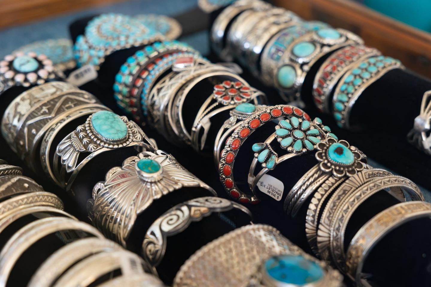 Silver bracelets with turquoise stones displayed on a black stand.