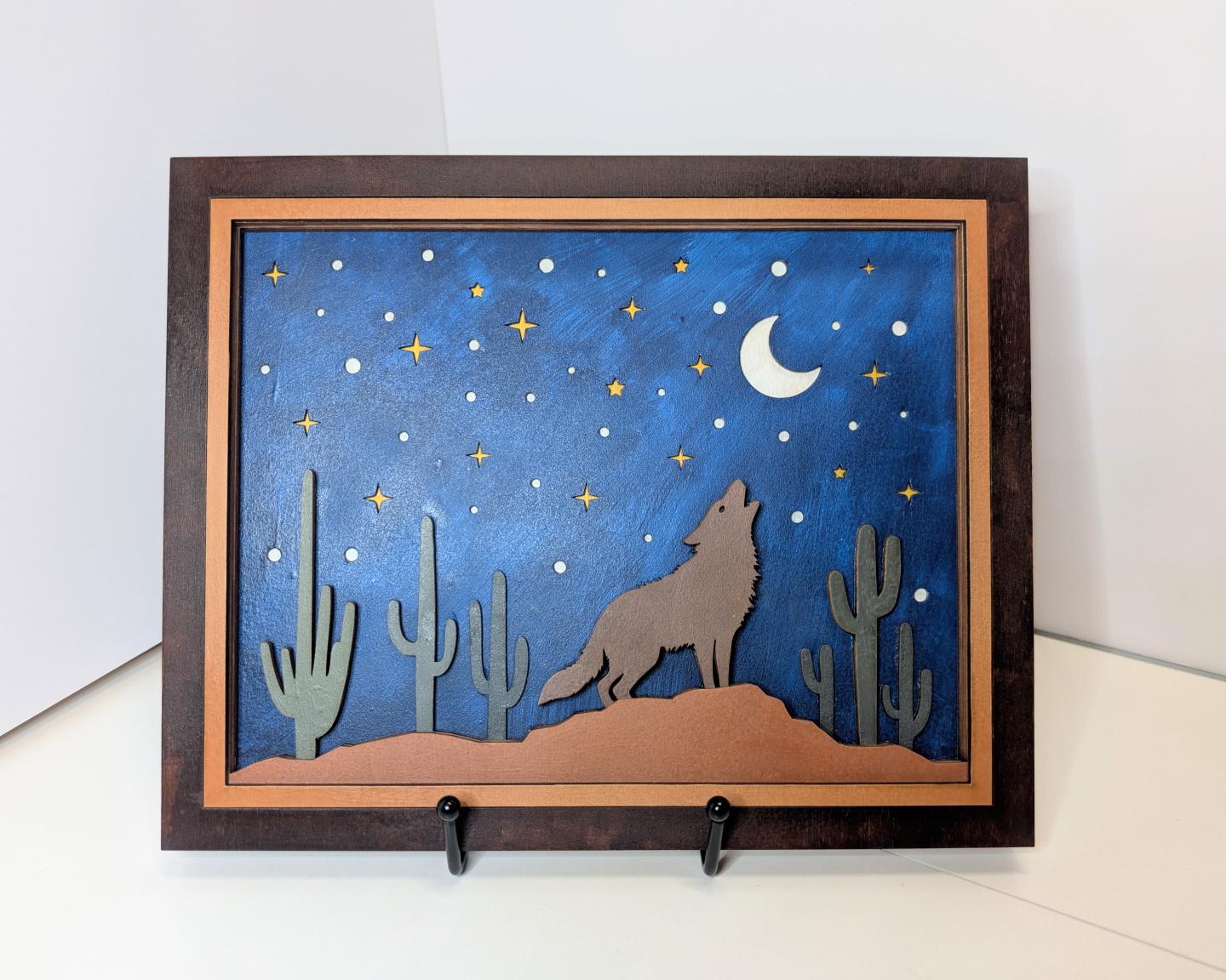 Wall art of a wolf howling at the moon with cacti and stars in a night sky.