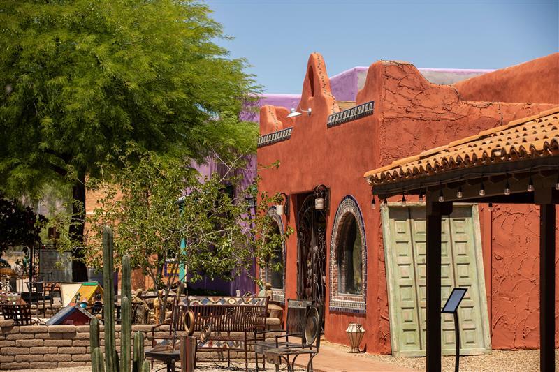 Desert courtyard with adobe buildings and cacti under a clear blue sky.