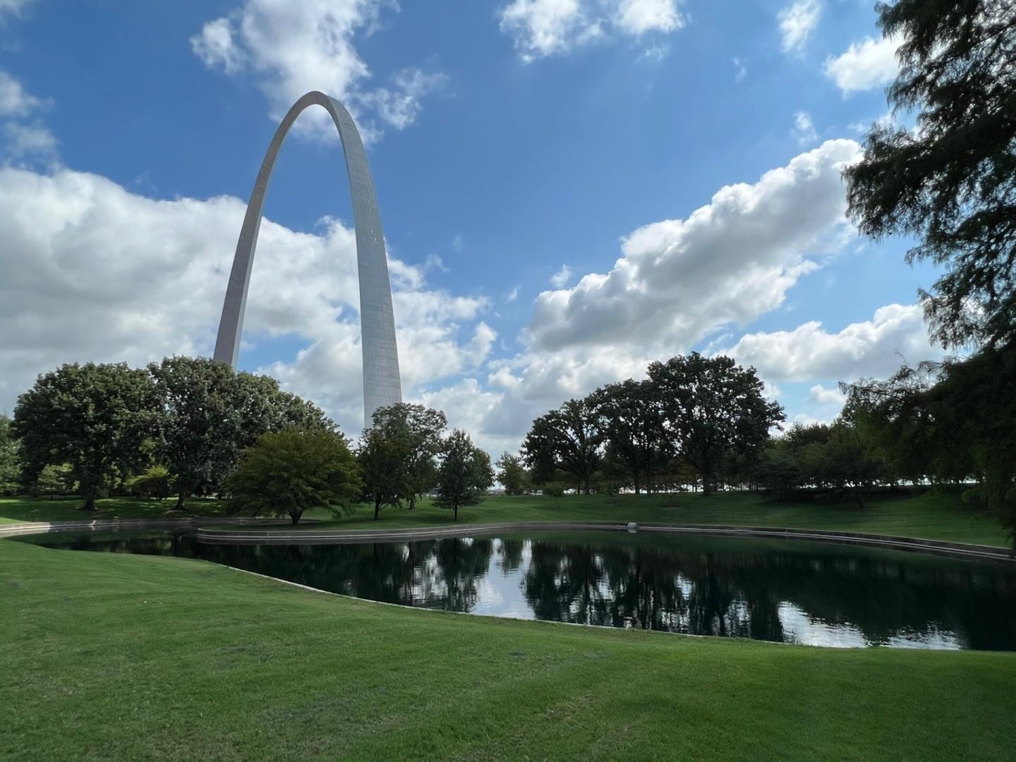 St. Louis Gateway Arch with a pond and trees, under a blue sky with clouds.