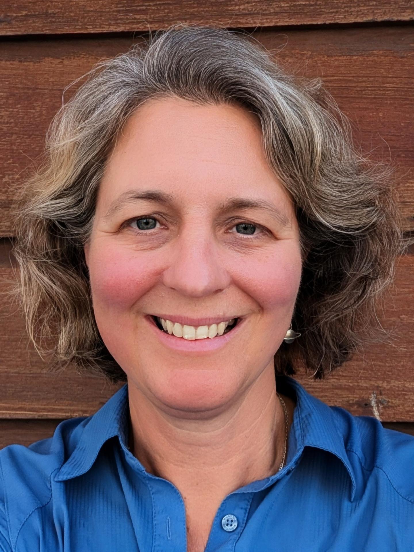 Smiling person with curly hair against a wooden wall.