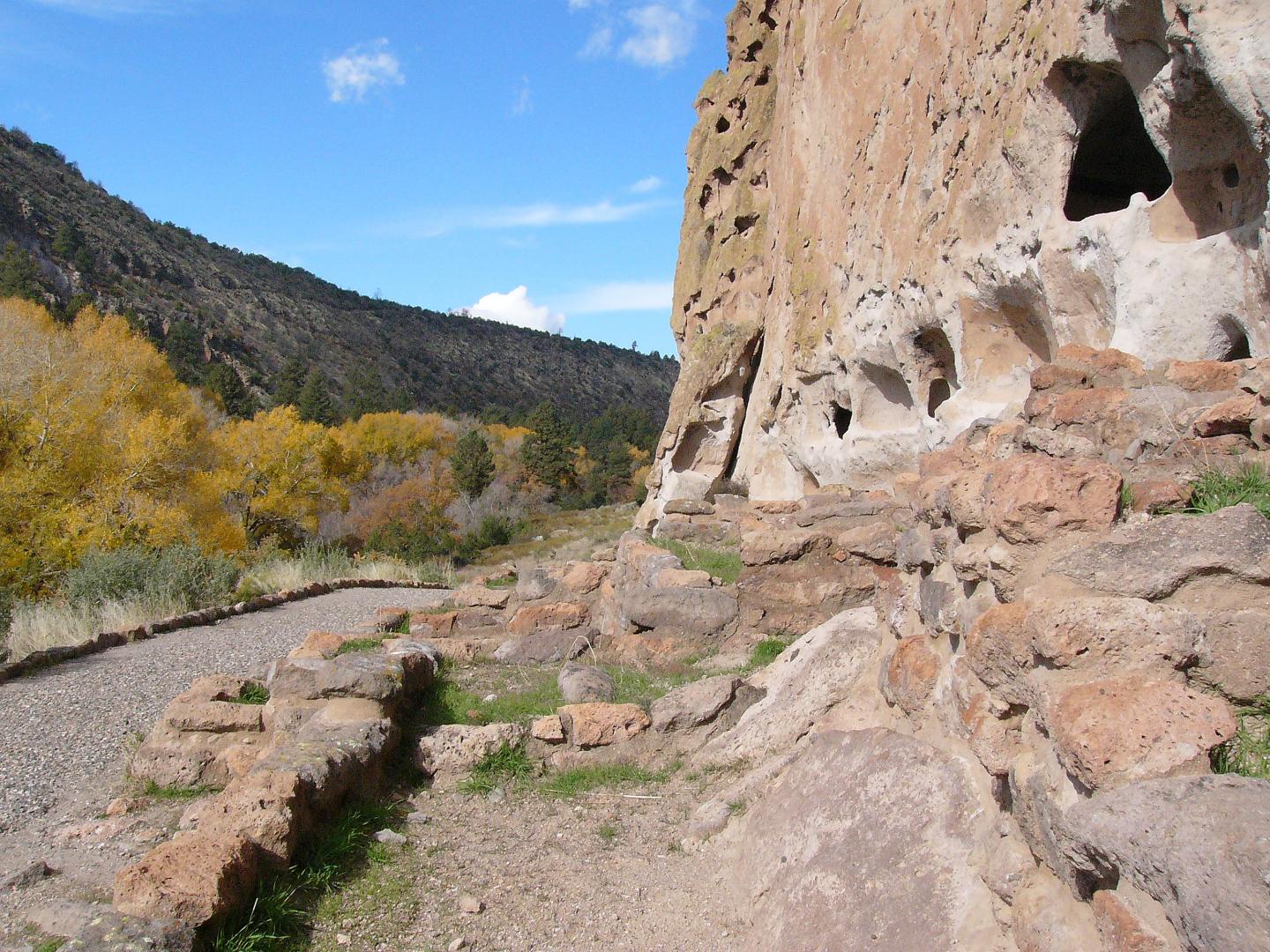 Path along a rocky cliff with blue sky and autumn trees.