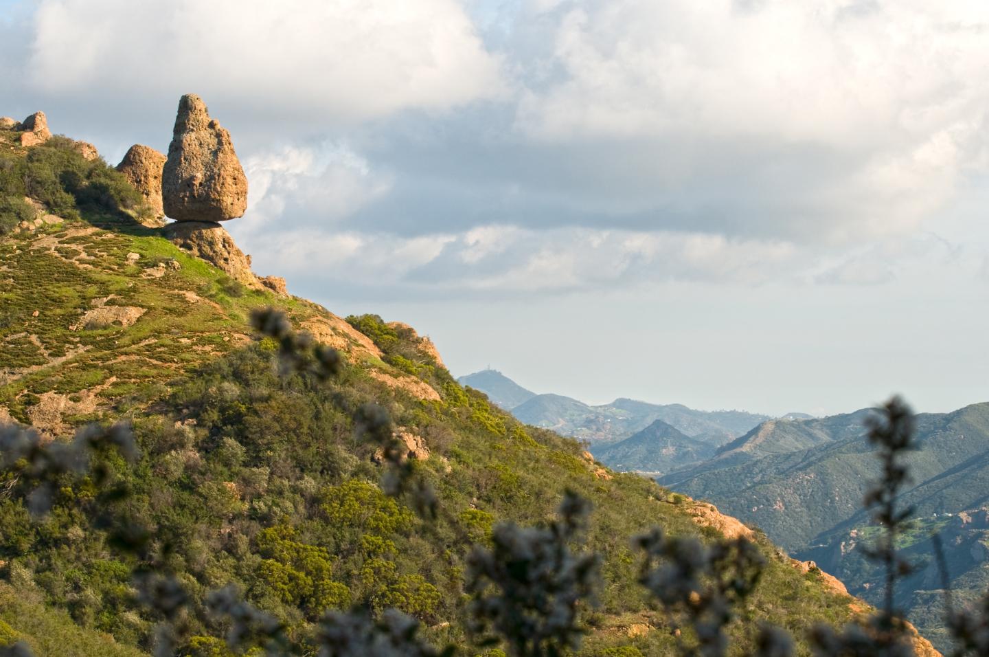 Rocky hillside with towering formation, cloudy sky, and distant mountains.