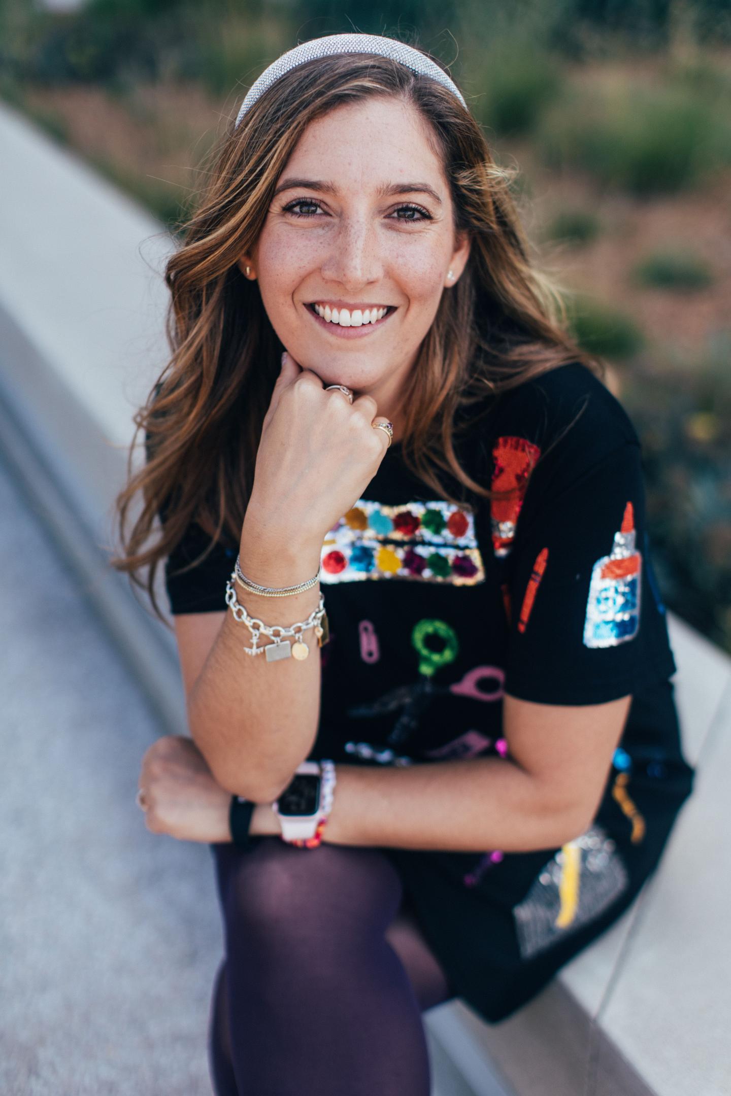 Smiling woman sitting outdoors, wearing a colorful dress.