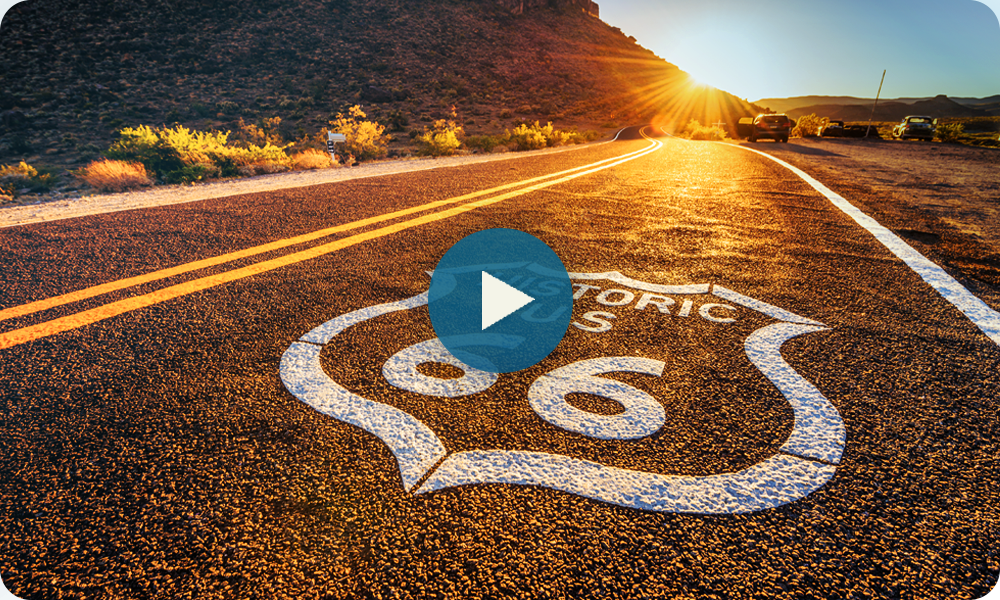 Historic Route 66 sign on sunlit road at sunset.