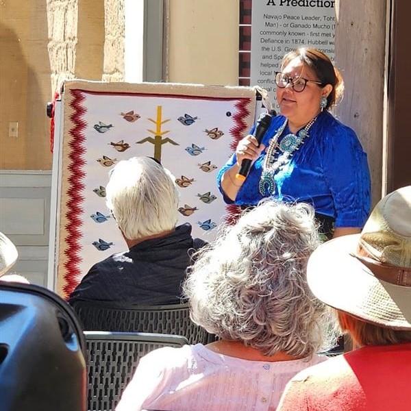 Diné weaver Tonita Yazzie in blue shirt talks to seated audience outdoors.