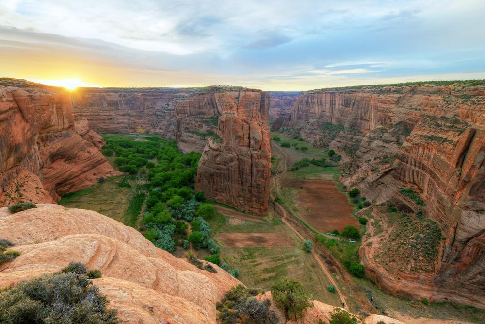 Canyon at sunset with green valley and red rock cliffs.