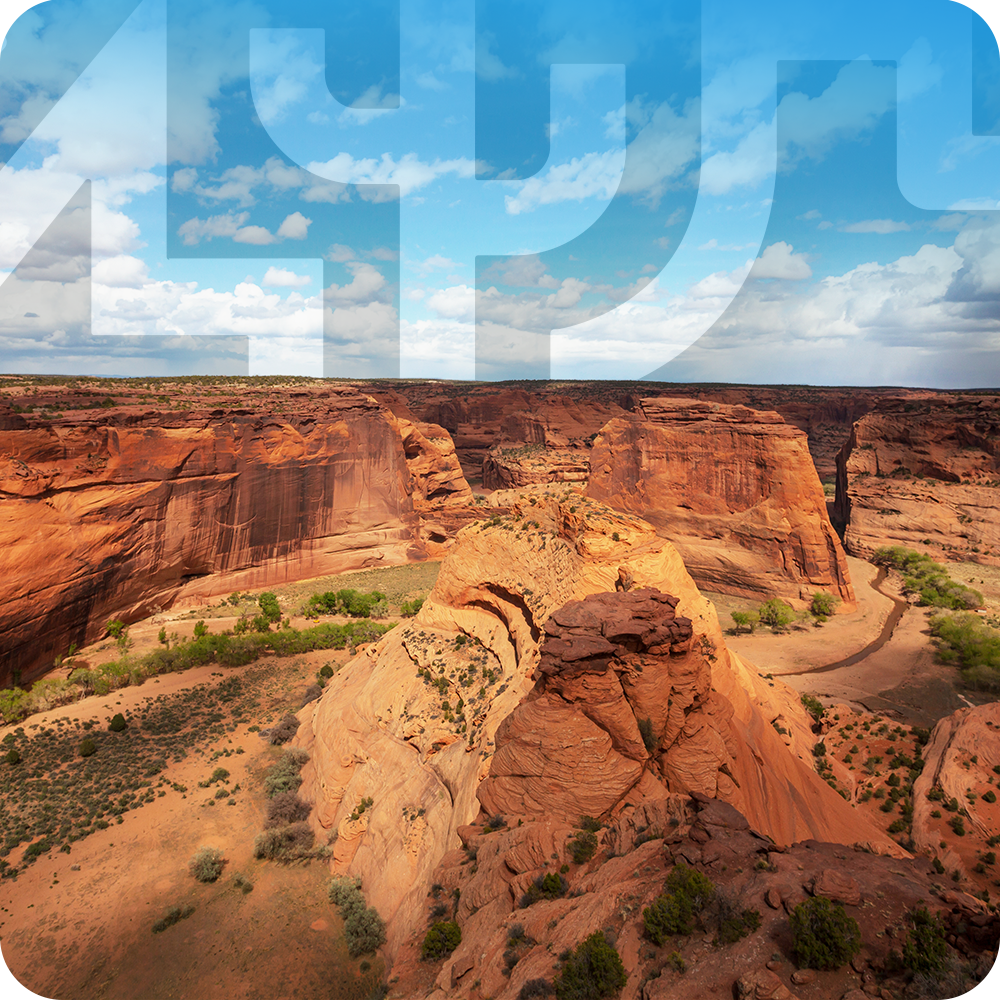 Canyon with red rock formations under a blue sky with clouds.