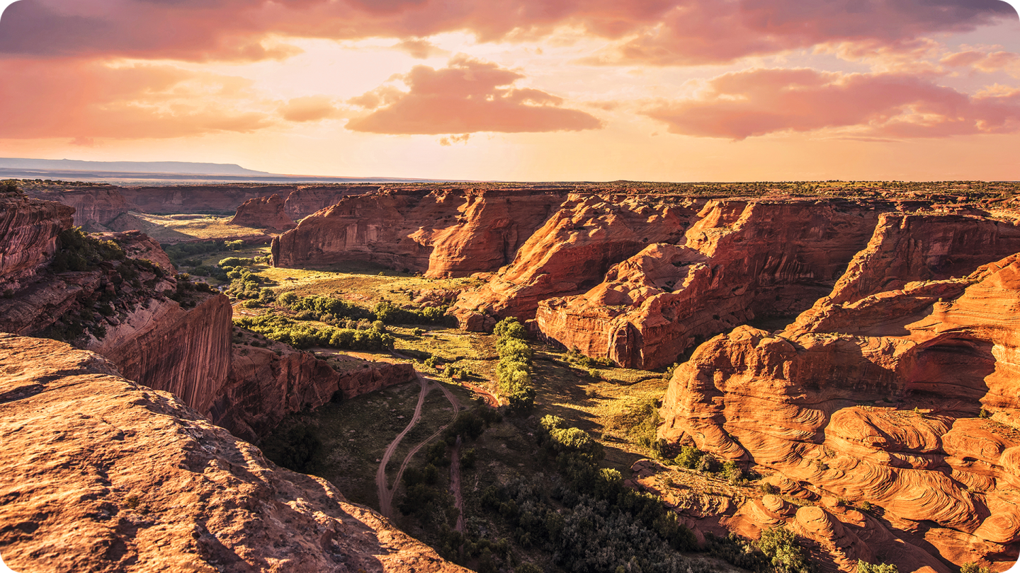 Canyon at sunset with red rock formations and cloudy sky.