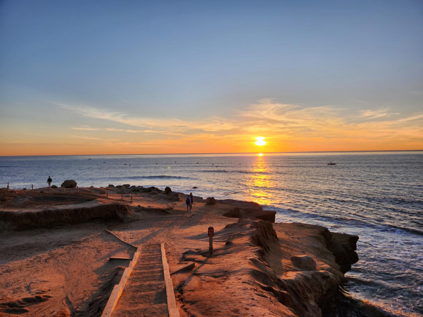 Sunset over a rocky coastline with a clear sky and calm ocean.