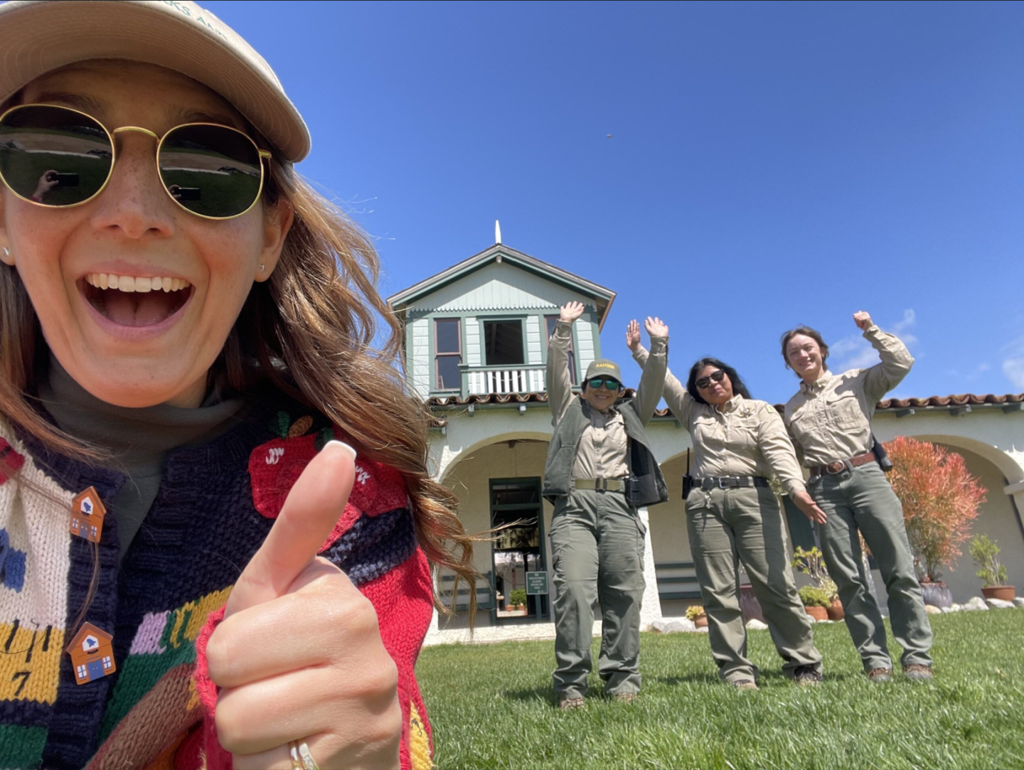 Woman smiling with thumbs up, three people waving in front of a house.
