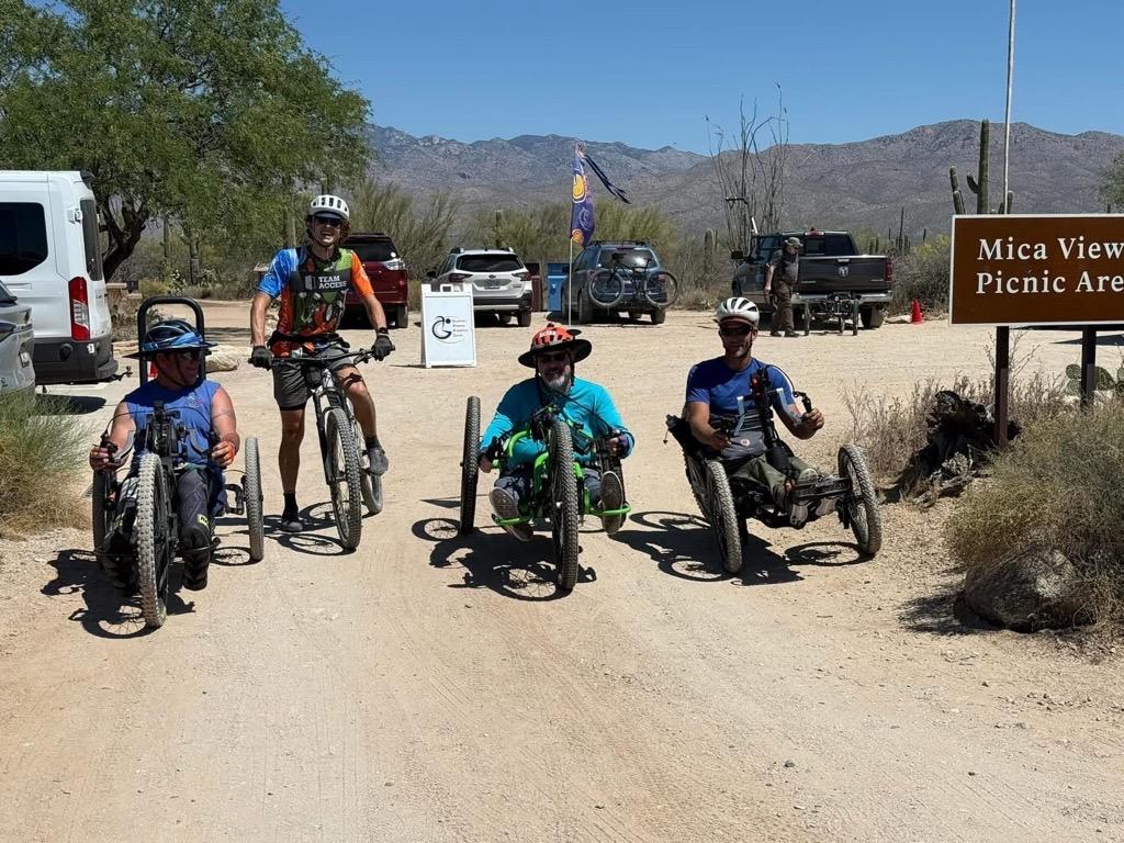 Four people on adaptive bikes on a sunny desert trail.