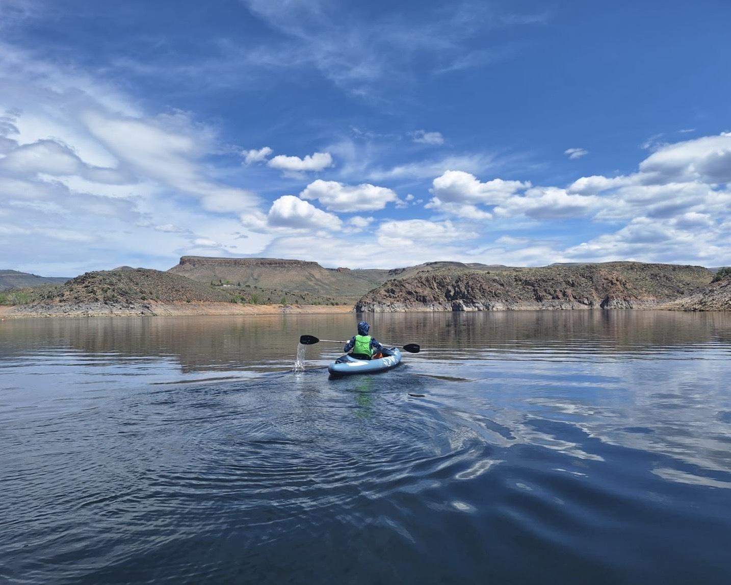 Kayaker on a calm lake under a blue sky with scattered clouds.