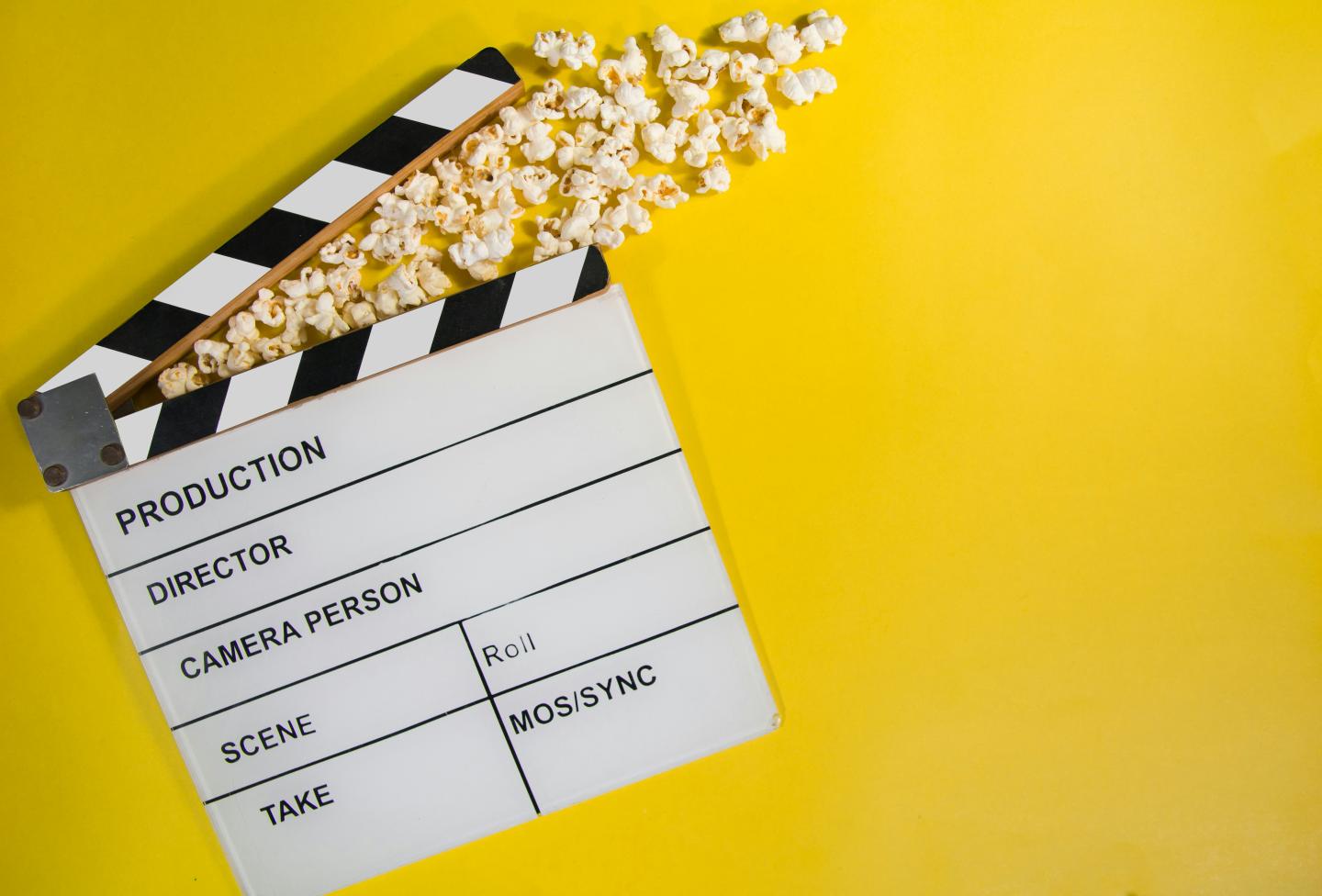 Film clapperboard and popcorn on a yellow background.