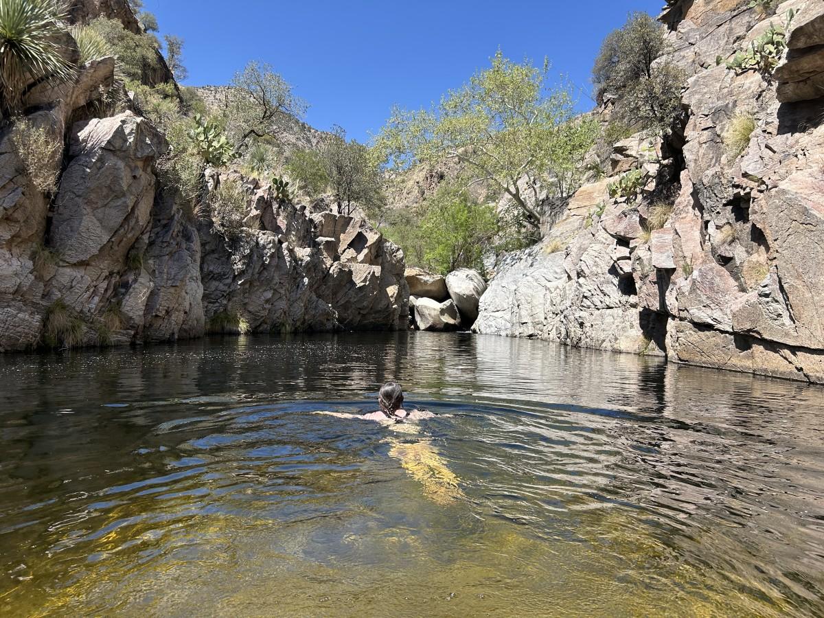 Swimmer in a rocky pool under a clear blue sky.