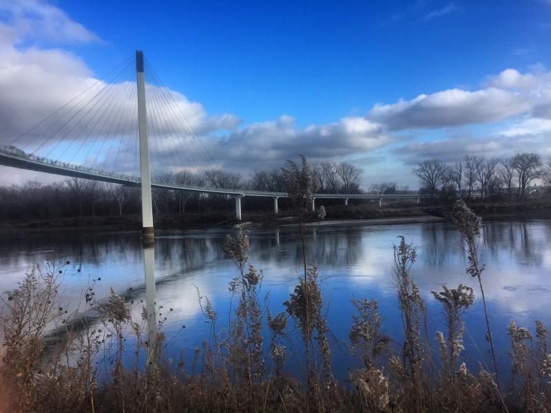 Bridge over calm river, with blue sky and clouds reflecting on water.
