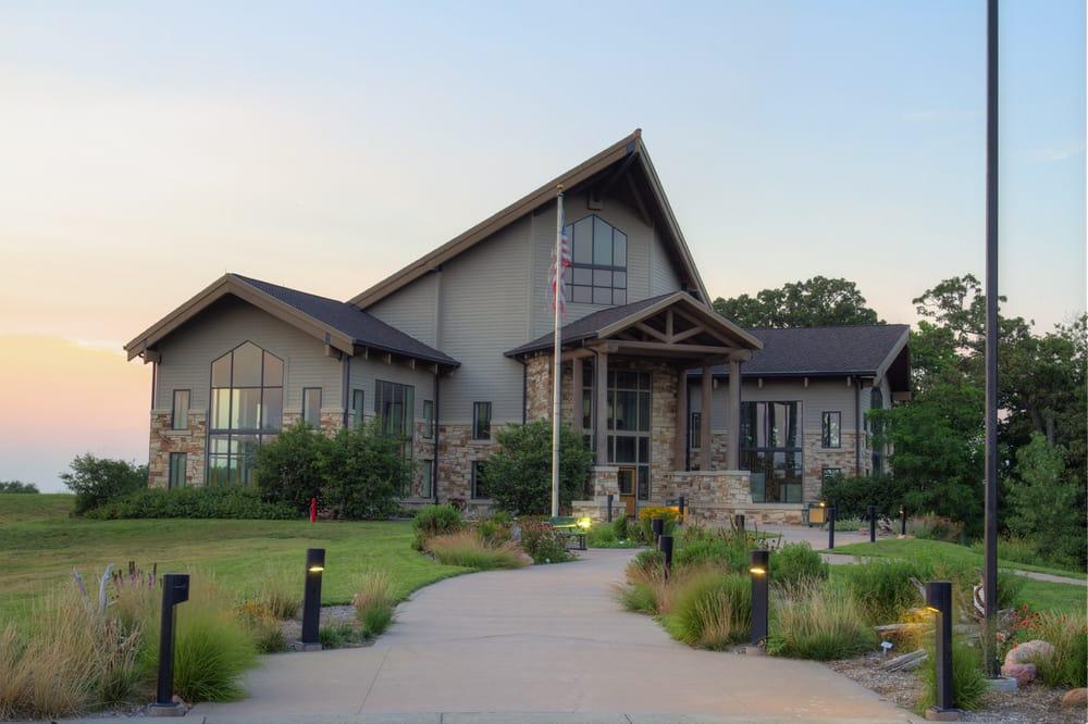 Modern building with peaked roof at sunset, surrounded by grass and a path.