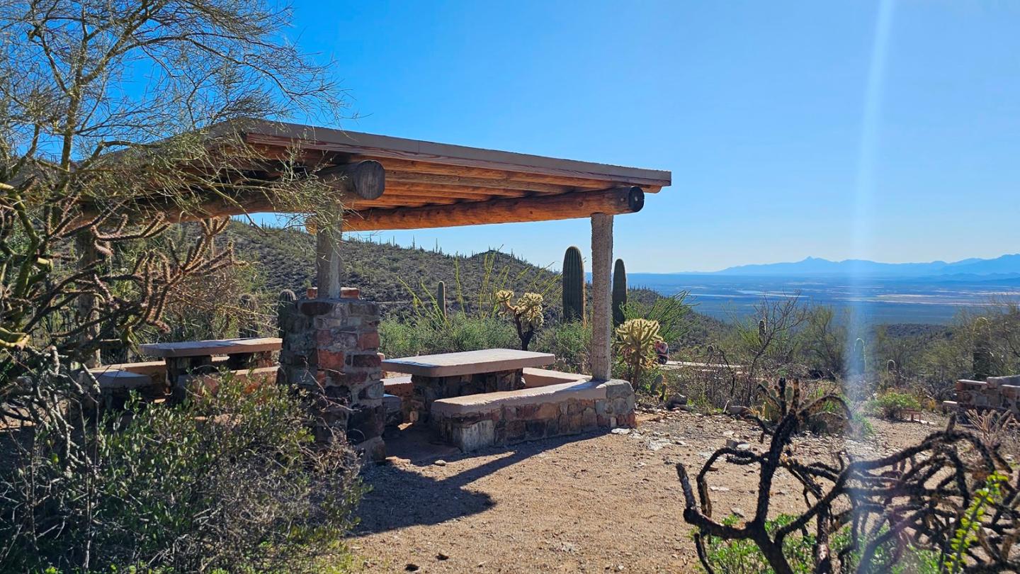 Desert picnic area with wooden shelter, tables, and distant mountain view.