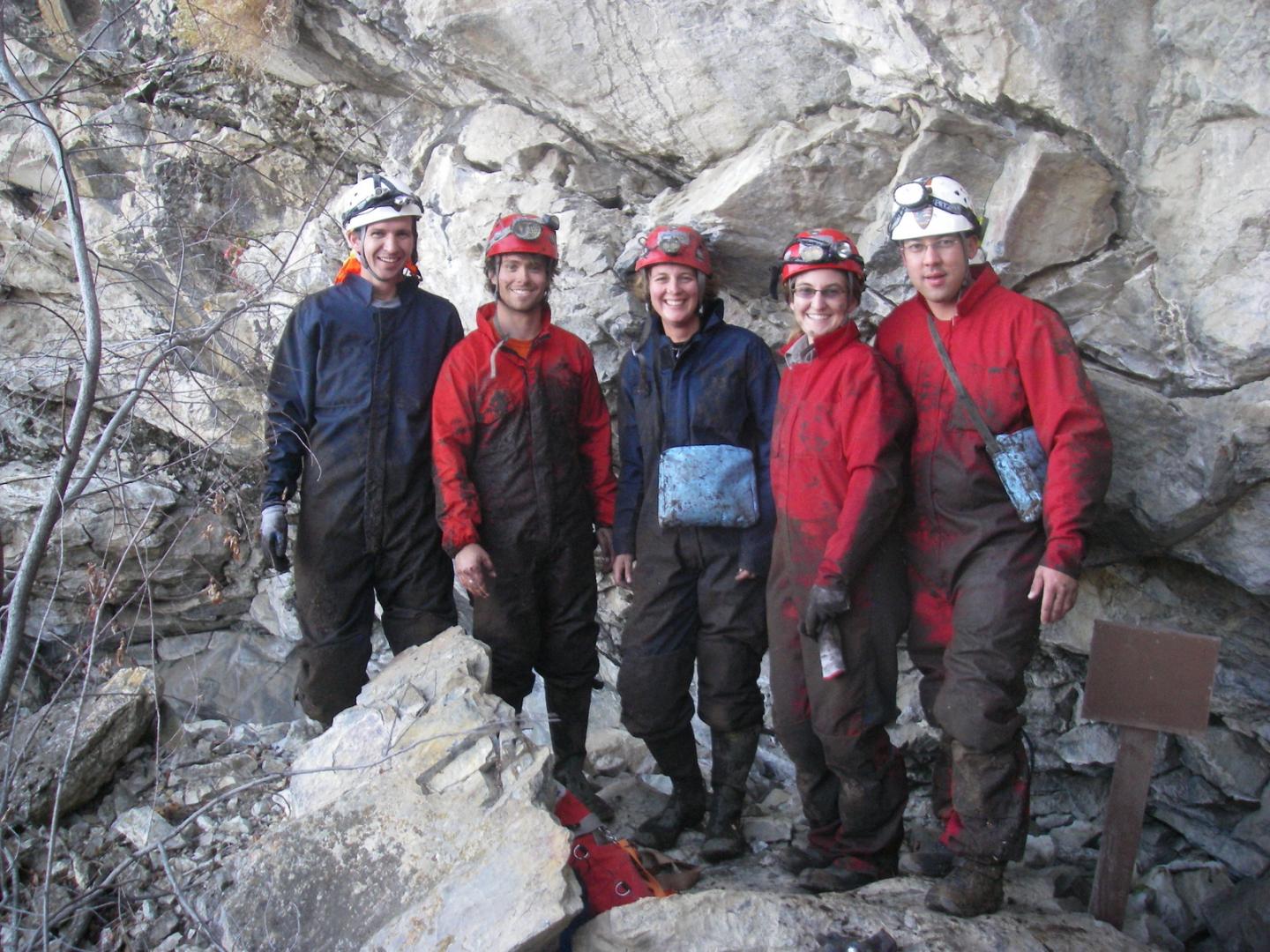 Five people in caving gear pose in front of a rocky background.