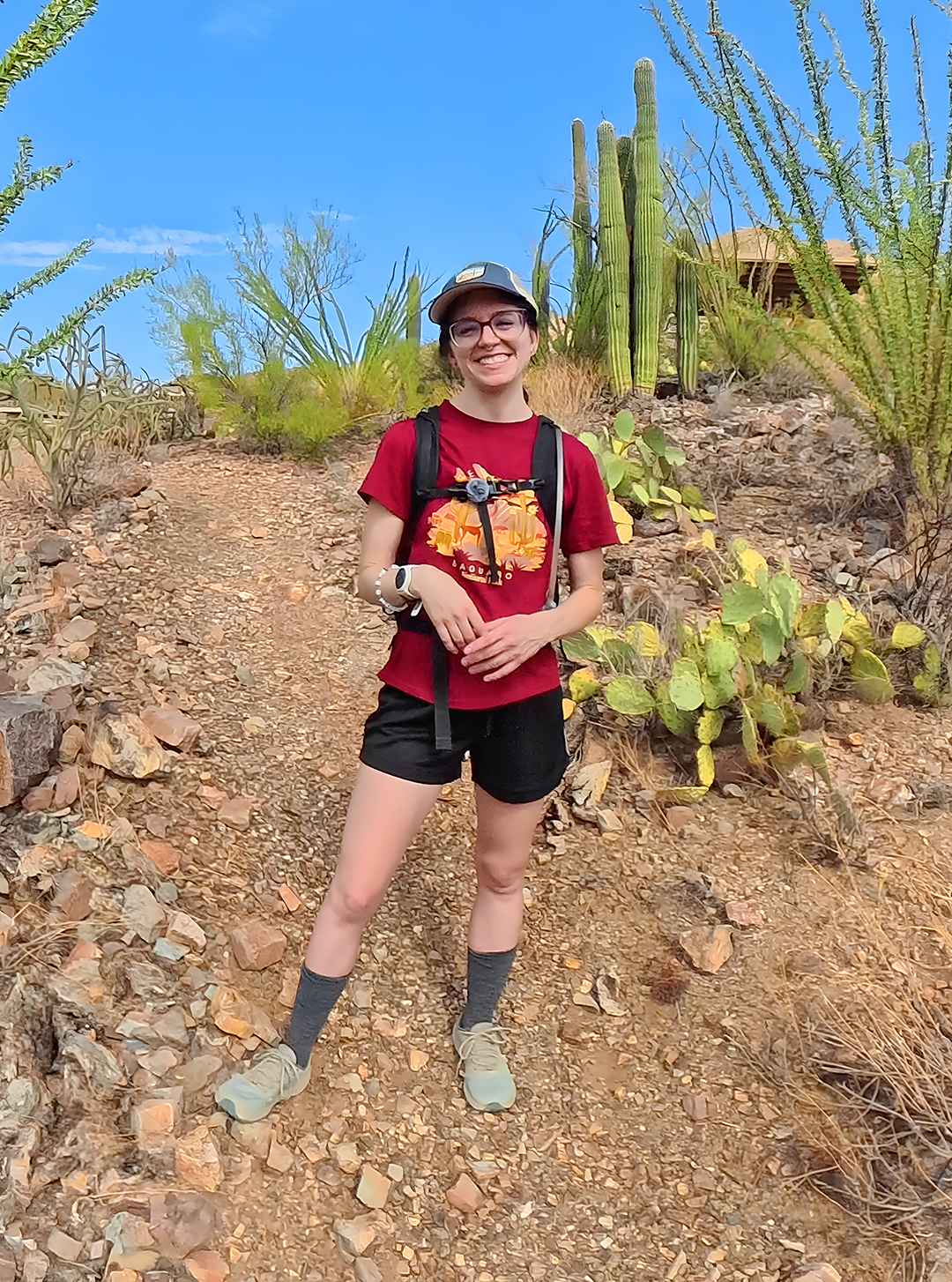 Young woman hiking on a rocky desert trail, smiling, with cacti in the background.