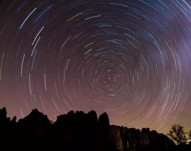 Star trails circling above jagged mountains at dusk.