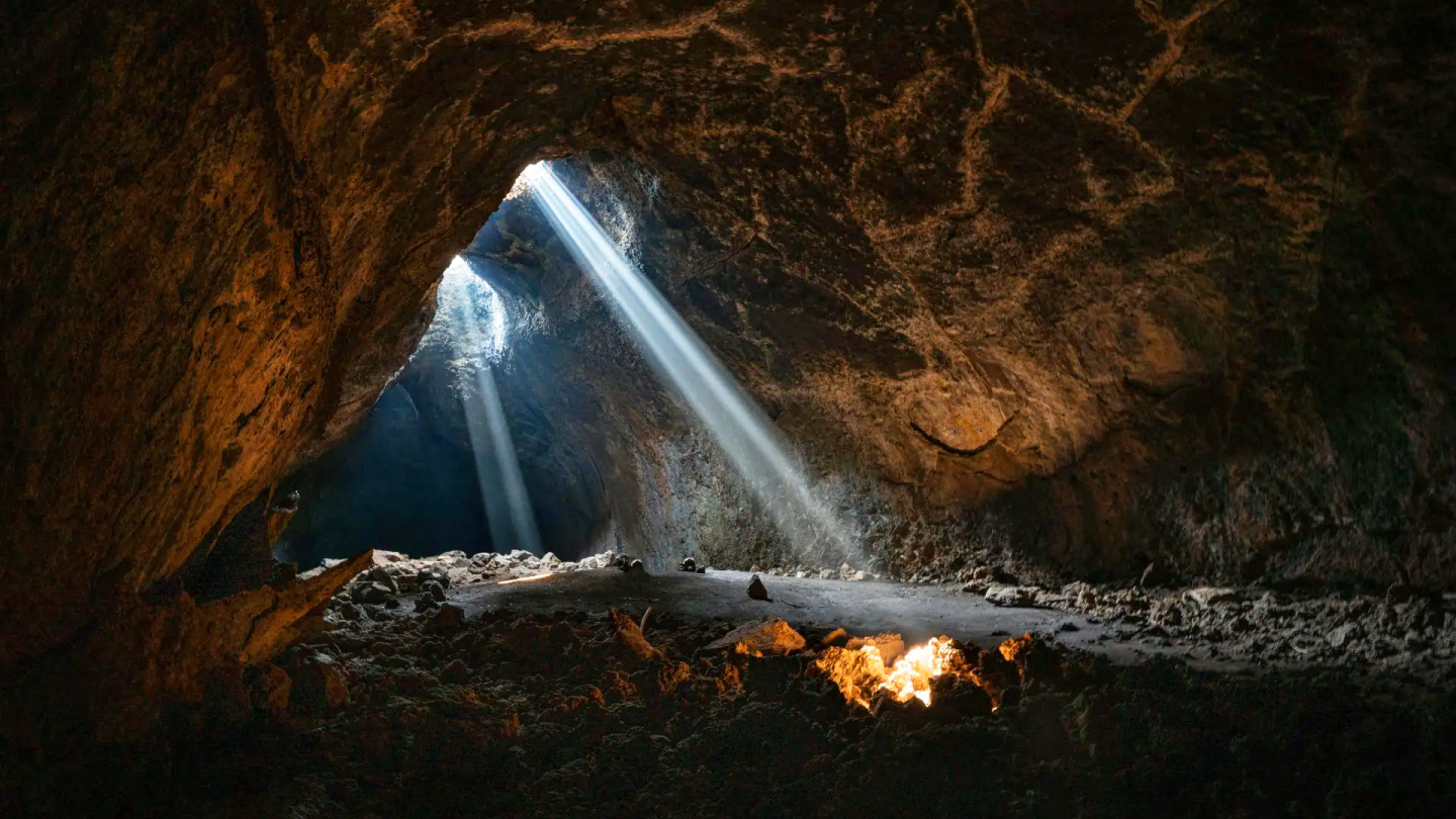 Sunlight beams through cave opening onto rocky floor.