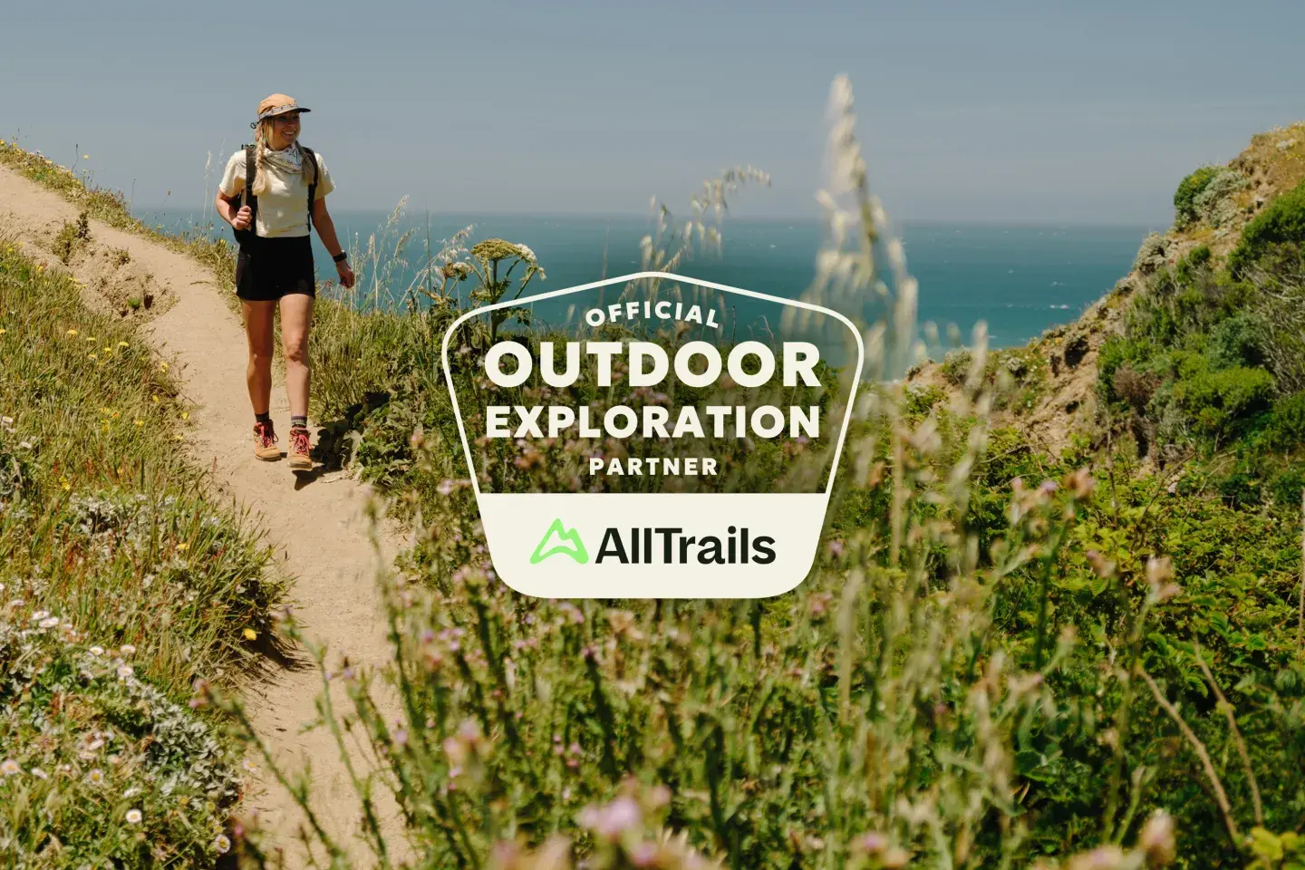 Hiker on a coastal trail with a logo for AllTrails partnership.
