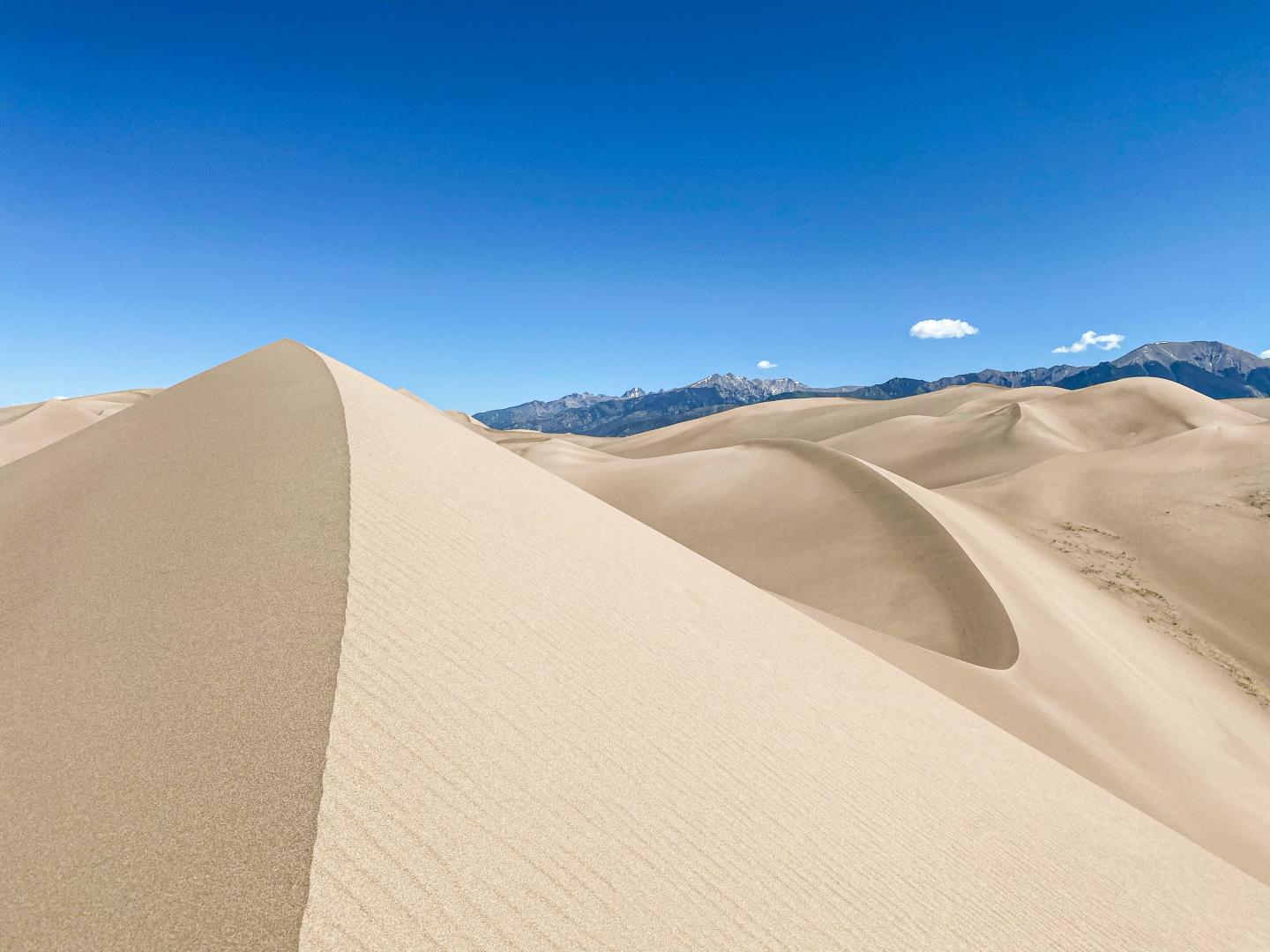 Sand dunes under a clear blue sky at Great Sand Dunes, with distant mountains.