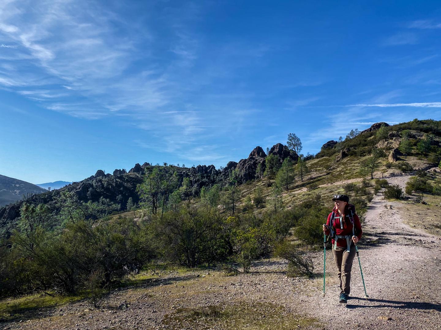 Hiker with poles on High Peaks Trail at Pinnacles National Park under a blue sky.