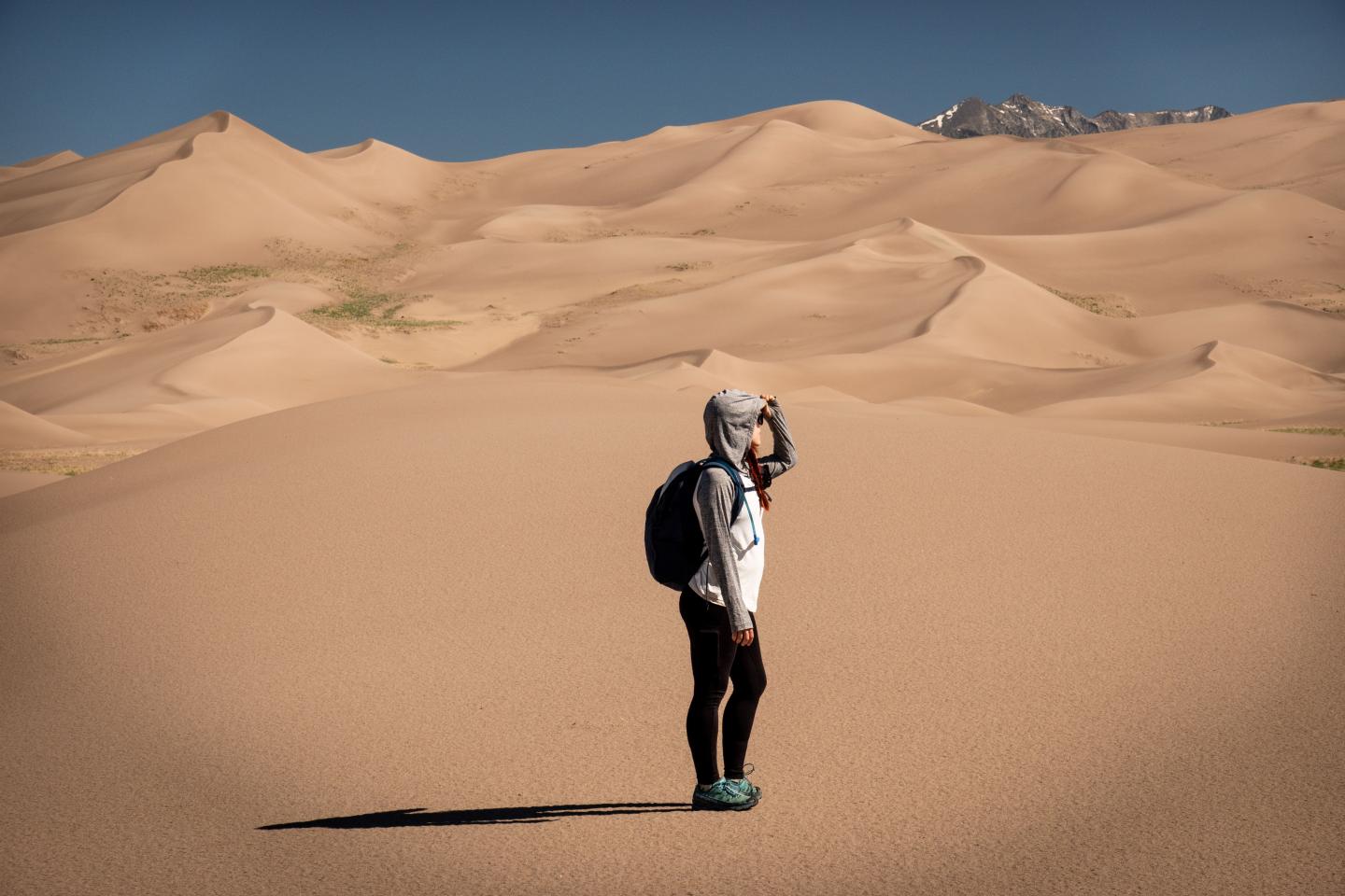 Person standing in the Star Dune at Great Sand Dunes, wearing a hood and backpack, surrounded by sand dunes.