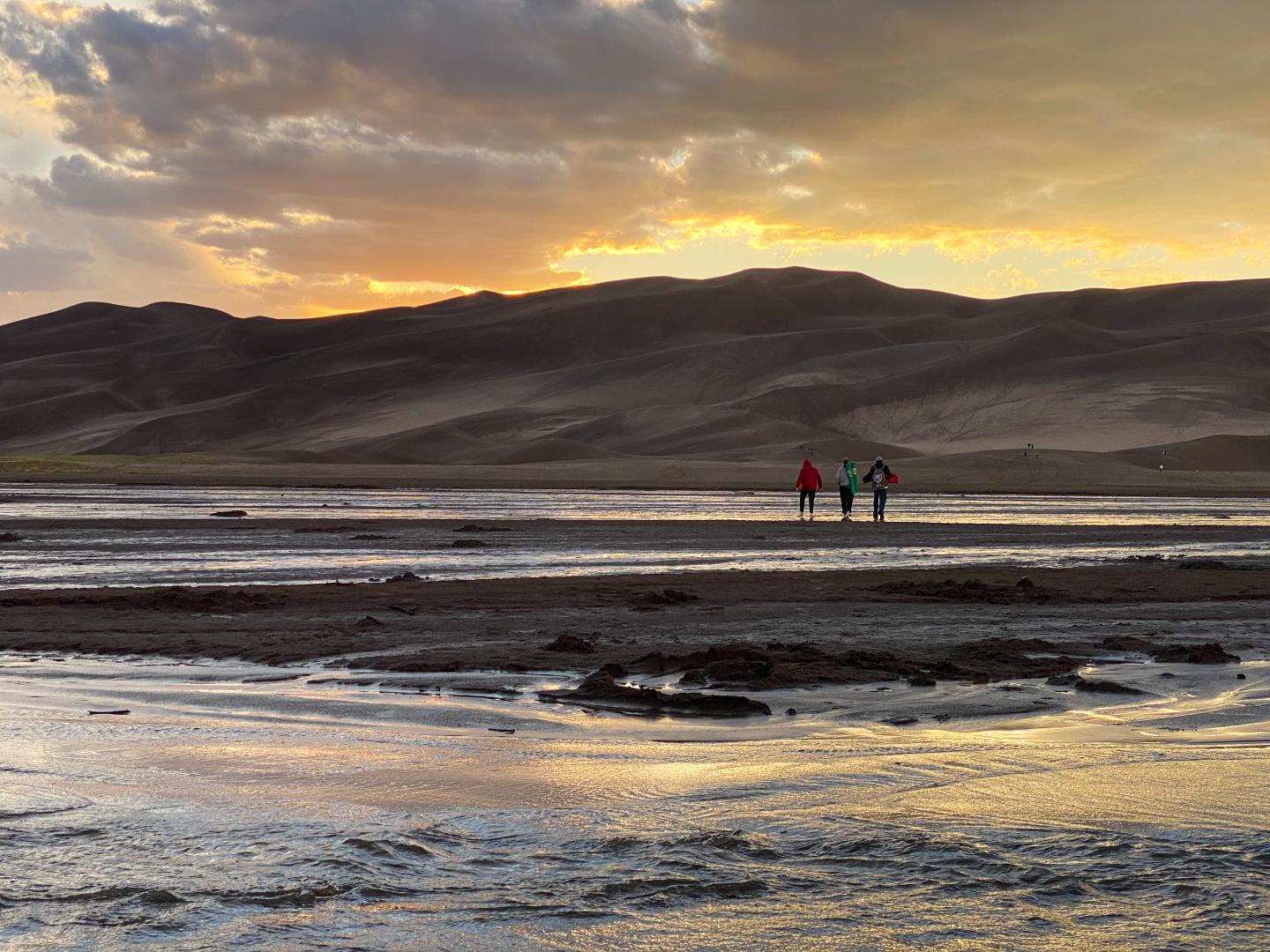 Sunset over desert hills, three people walking along a reflective water stream.