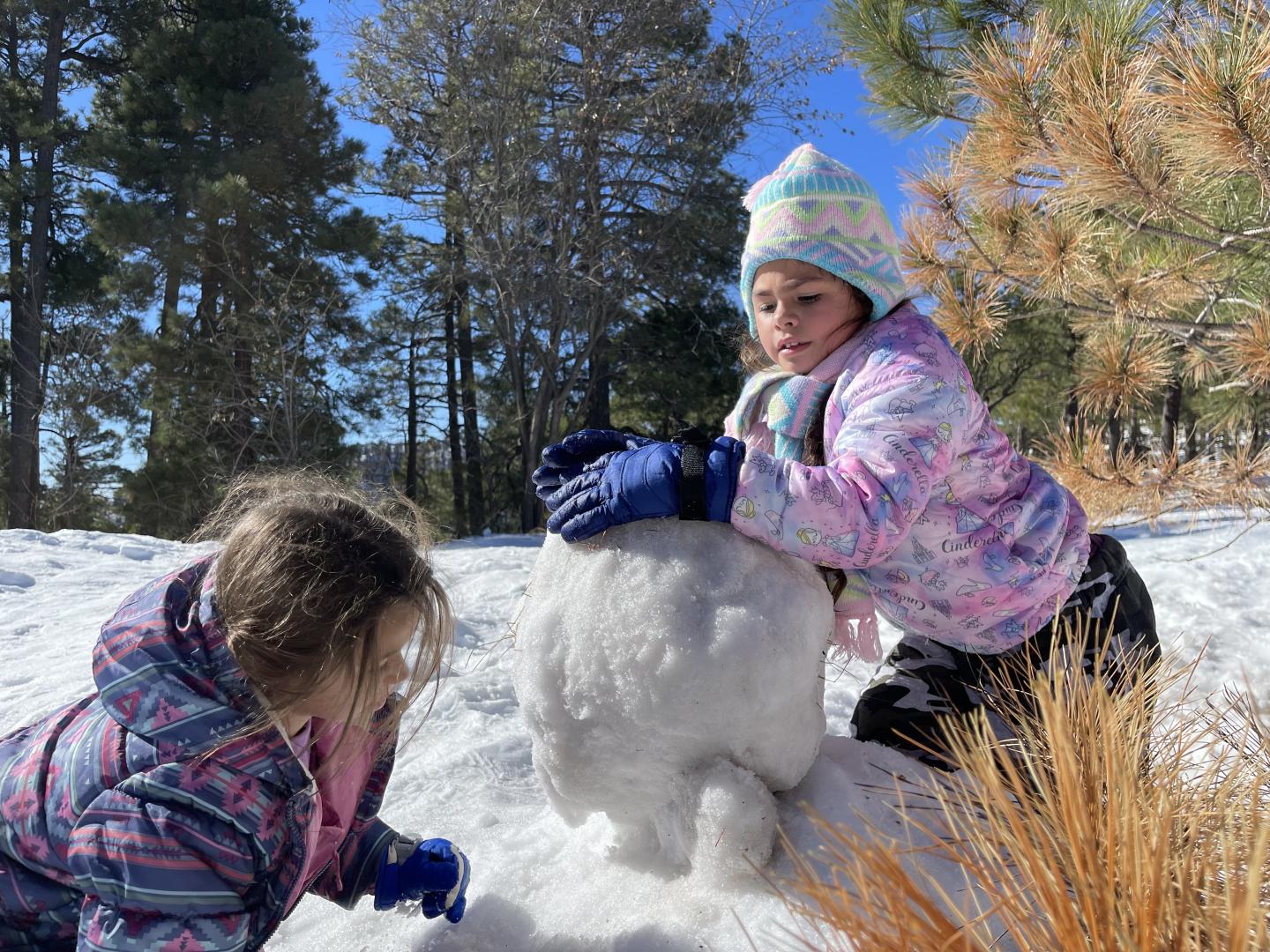 Two children build a snowman on Mt. Lemmon, wearing colorful winter clothes.