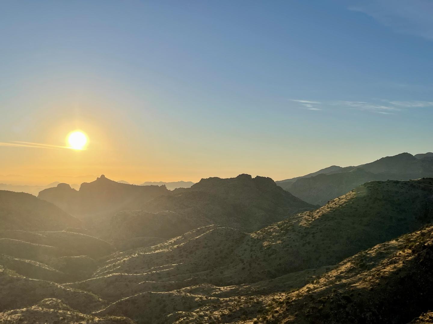 Sun setting over mountain range, casting glows on ridges.