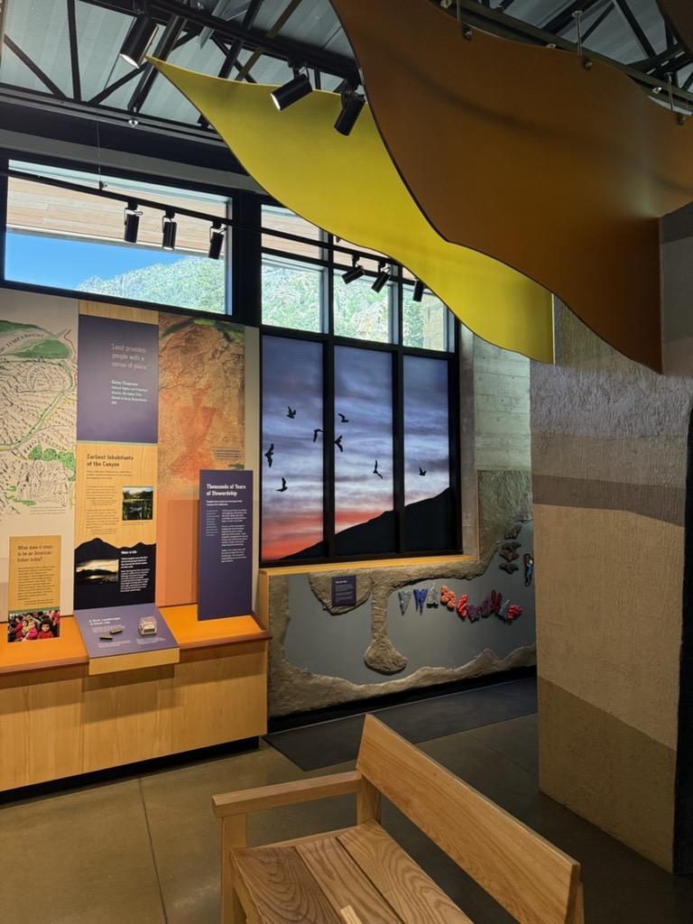 Timpanogos Cave exhibit with maps, panels, and a bench, under bright yellow and orange ceiling decor.