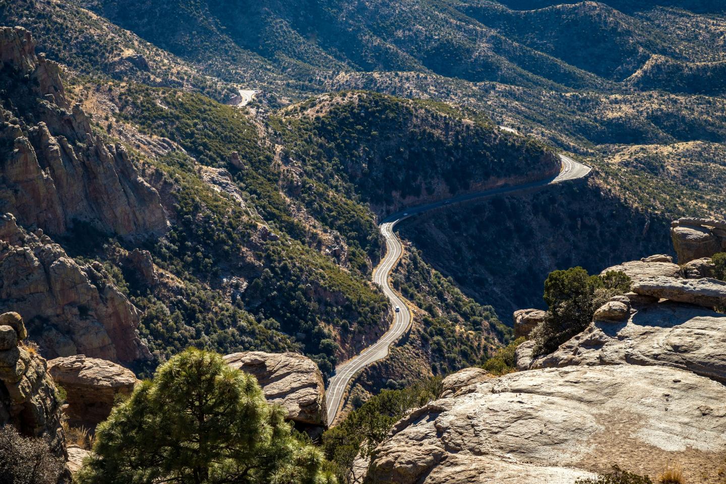 Winding mountain road through rocky landscape and green bushes.