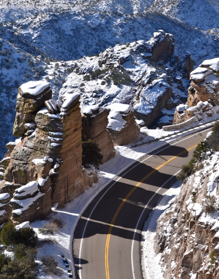 Winding mountain road with snow-covered rocks and hills.
