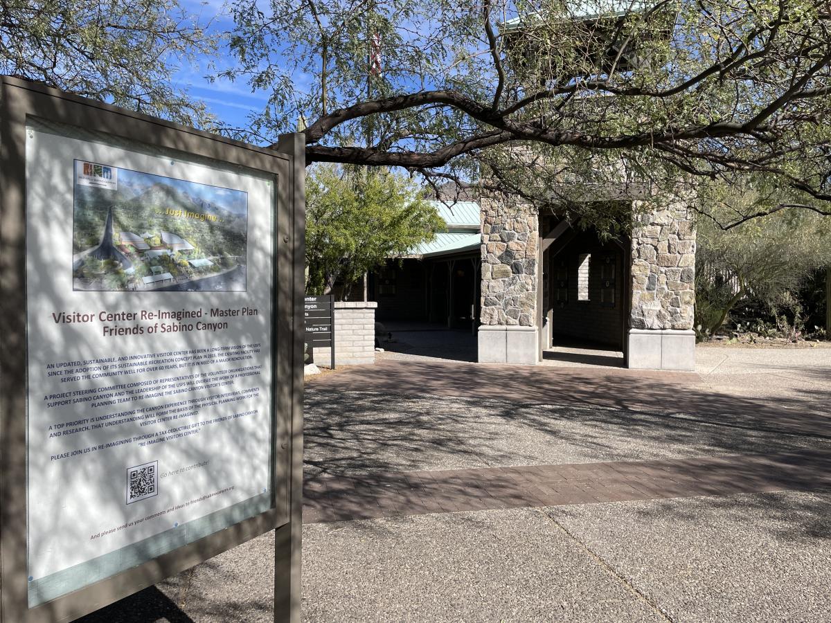 Pathway leading to a stone building with trees and informational sign nearby.