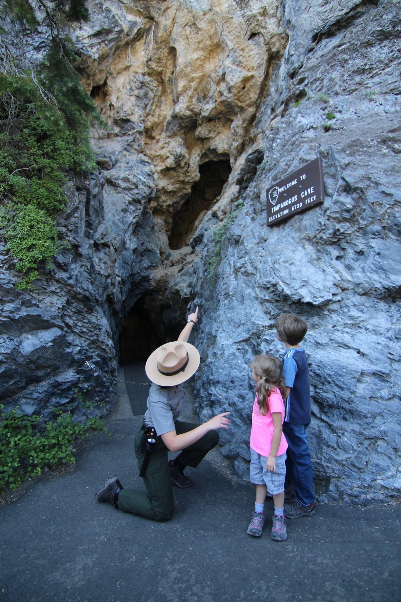 Park ranger showing a cave entrance to two children.